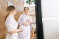 Cheerful female doctor and young colleague woman talking standing on staircase in medic clinic, smiling, laughing Royalty Free Stock Photo