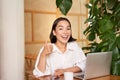 Cheerful female entrepreneur with laptop, showing thumbs up and sitting in cafe with coffee, approve, say yes Royalty Free Stock Photo