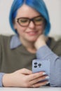 Young woman holding modern smart phone in hand. Cheerful white female with blue hair browing mobile app on a blue phone. Focus on