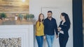 Cheerful realtor is meeting beautiful young couple in new house, opening door, showing documents and talking to clients Royalty Free Stock Photo
