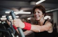 A cheerful female senior in gym doing cardio workout.