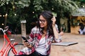 Cheerful female student playing with her dark hair. Outdoor portrait of blithesome girl holding pho