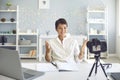 Cheerful female vlogger recording a video on camera sitting at her desk in home office