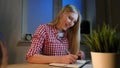 Cheerful female writing in daily planner. Lively young blond woman in casual checkered shirt sitting at wooden desk with