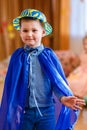 Cheerful five-year-old boy in a blue suit and hat dancing on a blurred background of kindergarten
