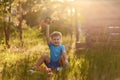 A cheerful five-year-old boy in a blue t-shirt and shorts plays with plastic cars in the summer sitting on the grass in the Park