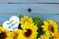 Cheerful floral with bright yellow silk sunflowers and a rustic blue washed plank background for Mother`s Day in May. A heart