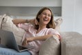 Cheerful freelancer woman working on home couch, holding laptop