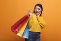 Cheerful friendly fashionable shopper smiling while carrying shopping bags and wearing yellow trendy sweater.