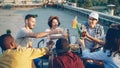 Cheerful friends are chatting and drinking lemonade sitting on rooftop on warm sunny day with snacks and drinks on table Royalty Free Stock Photo