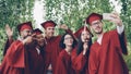 Cheerful friends graduating students are taking selfie with smartphone, young people are posing, showing hand gestures