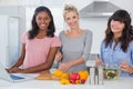 Cheerful friends making salad and using laptop for recipe looking at camera Royalty Free Stock Photo