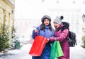Cheerful friends with paper bags on eve. Happy women do Christmas shopping. Surprised funny girls on winter city street Royalty Free Stock Photo
