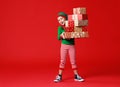 Cheerful funny baby in Christmas elf costume with gifts on red background