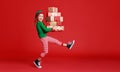 Cheerful funny child in Christmas elf costume with gifts on red background