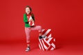 Cheerful funny child in Christmas elf costume with gifts on red background