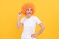 cheerful funny girl with fancy look wearing orange hair wig on yellow background, cool