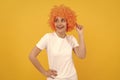 cheerful funny girl with fancy look wearing orange hair wig on yellow background, cool