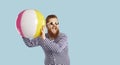 Cheerful funny guy in sunglasses playing with beach inflatable ball on pastel blue background. Royalty Free Stock Photo