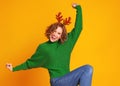 Cheerful happy woman with christmas deer antlers dances and enjoys life a colored yellow background