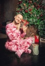 Cheerful funny man in pink sleepwear near decorated fir tree and hold Christmas present Royalty Free Stock Photo