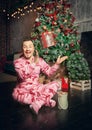 Cheerful funny man in pink sleepwear near decorated fir tree and throws up Christmas present