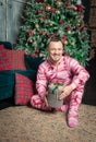 Cheerful funny man in sleepwear sitting on the floor near decorated fir tree and Christmas present Royalty Free Stock Photo
