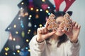 Cheerful funny woman cover her eyes with x-mas gingerbread fir shaped cookies and having fun near alternative christmas tree.