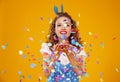 Cheerful funny young woman with festive confetti on yellow