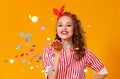 Cheerful funny young woman with festive confetti on yellow