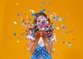 Cheerful funny young woman with festive confetti on yellow