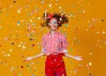 Cheerful funny young woman with festive confetti on yellow