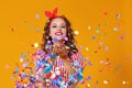 Cheerful funny young woman with festive confetti on yellow