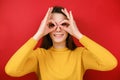 Cheerful funny young woman having fun making glasses shape with hands, does funny face with eyes wide open Royalty Free Stock Photo