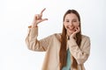 Cheerful gen-z girl showing small size tiny thing, smiling pleased, demonstrate something on copy space, showing little Royalty Free Stock Photo