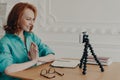 Cheerful ginger European woman sits in front of cellular camera, records self presentation video, shares professional skills,