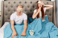 Cheerful ginger girl yawning while sitting on bed with her sleepy husband Royalty Free Stock Photo