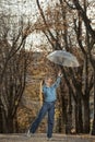 Cheerful girl in blue sweater and pants with transparent umbrella on alley. Beautiful woman dance in autumn park Royalty Free Stock Photo