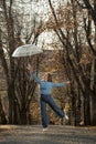 Cheerful girl in blue sweater is photographed with transparent umbrella on alley. Autumn park and beautiful woman Royalty Free Stock Photo