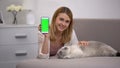 Cheerful girl with cat holding smartphone, green screen for animal charity site