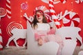 A cheerful girl in glasses with a red nose and horns is holding a candy in her hands. A wall of lollipops. The child is sitting in