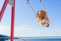 Cheerful girl in a hat and dress riding on a swing overlooking the sea.