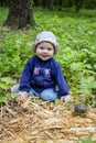 Cheerful girl in a hat exploring fallen trees in the forest. Baby 9 months in the forest, soft focus child portrait