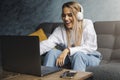 Cheerful girl in headphones sitting on sofa in front of laptop. Entertainment online content for streaming at affordable