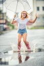 Cheerful girl jumping with white umbrella in dotted red galoshes. Hot summer day after the rain woman jumping and splashing in