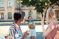 Cheerful girl meeting her friends in the university yard.