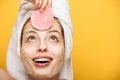 Cheerful girl with moisturizing facial mask looking at cosmetic sponge