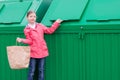 A cheerful girl in a pink jacket, carries a paper bag, in a green garbage container to throw it away, there is a place for the Royalty Free Stock Photo