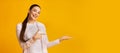 Cheerful Girl Pointing Finger Holding Something On Yellow Background