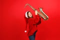 Cheerful girl with a saxophone on a red background, Christmas party